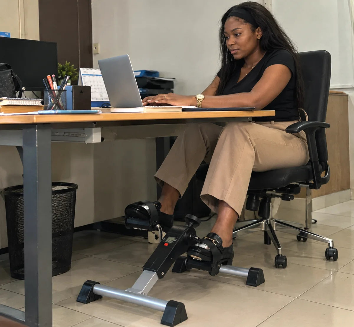 Femme au bureau qui travaille sur son ordinateur portable en pédalant avec le mini vélo KINETIX